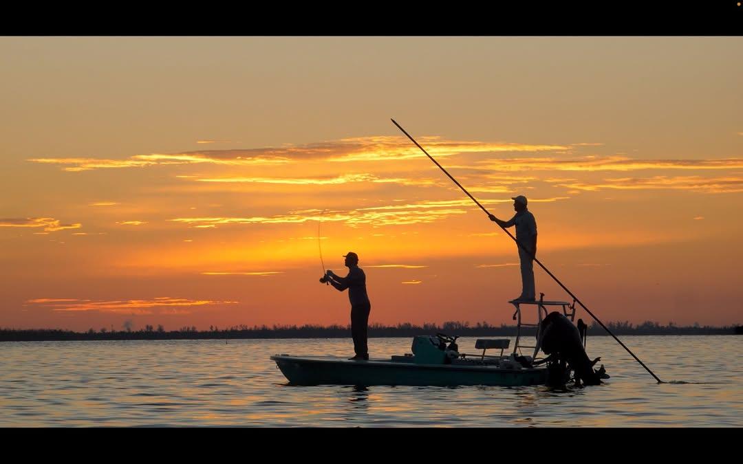 Fly angler casting from a flats skiff at sunrise while the guide poles
